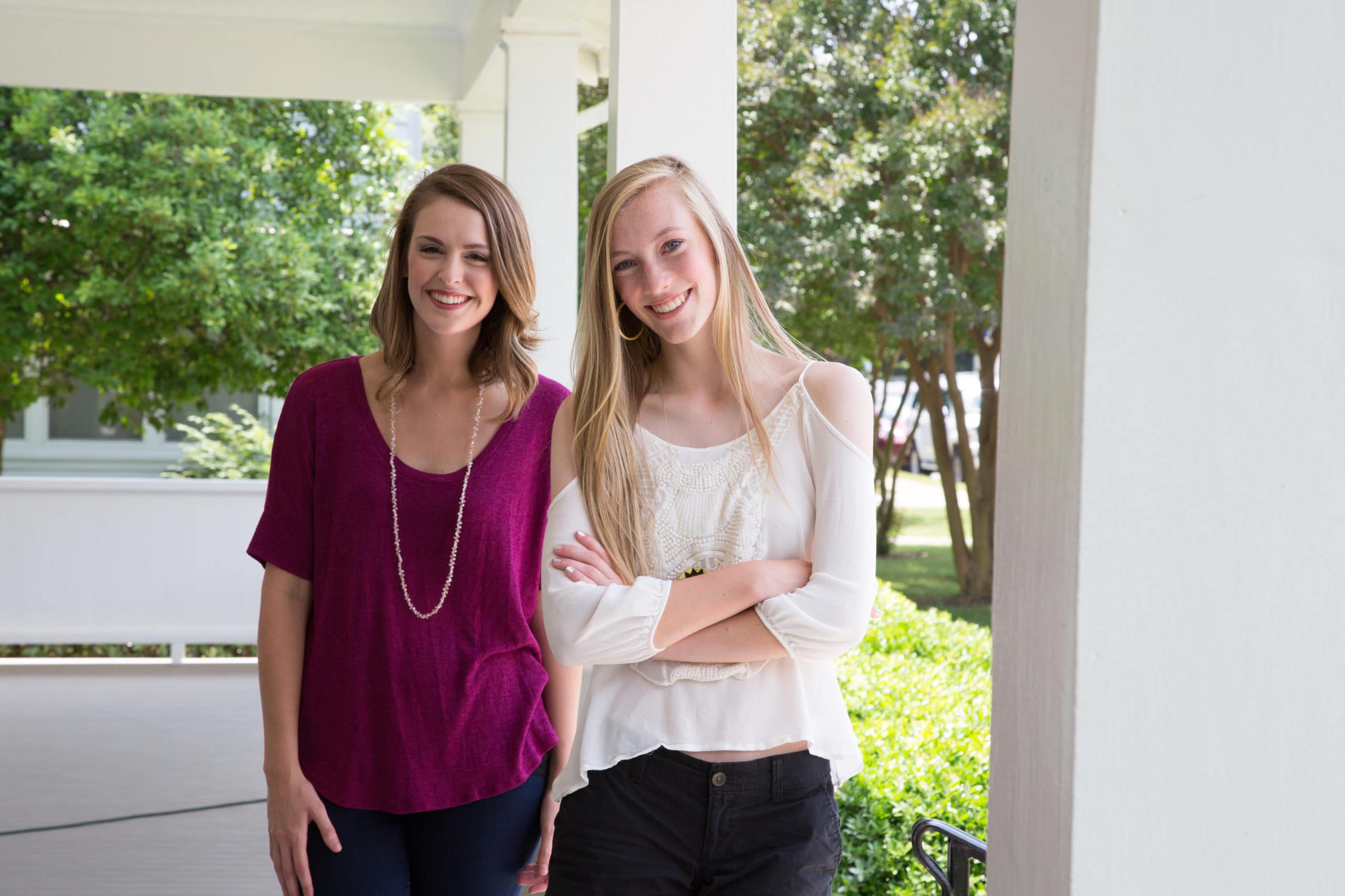 Two teen girls smiling and standing on a porch.