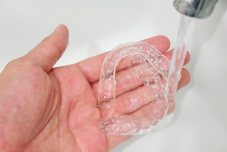 A hand holding clear aligners and cleaning them under a faucet.